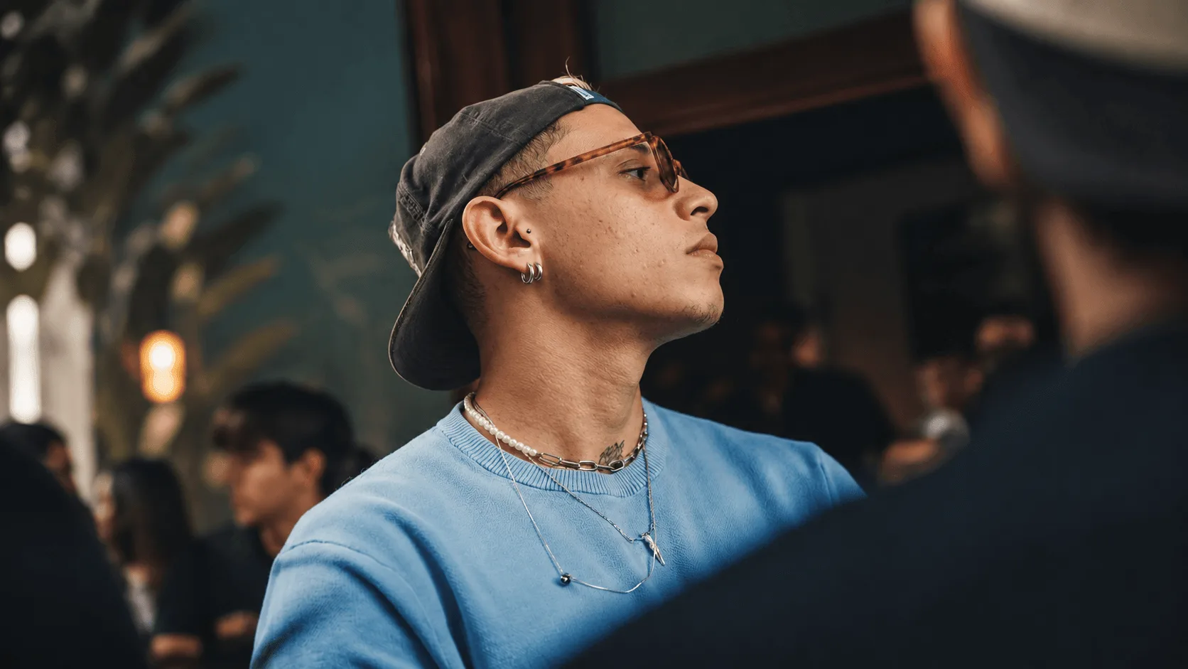 Breno Luis de boné, óculos e moletom azul, olhando para o lado